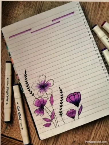A notebook featuring a creative front page design with purple flowers and colorful markers arranged on top.