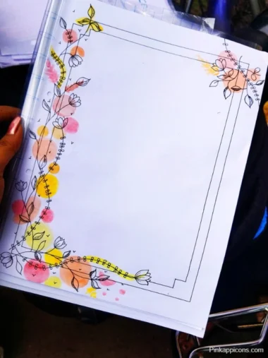 A person holds a handmade project front page featuring a colorful flower design on a piece of paper.
